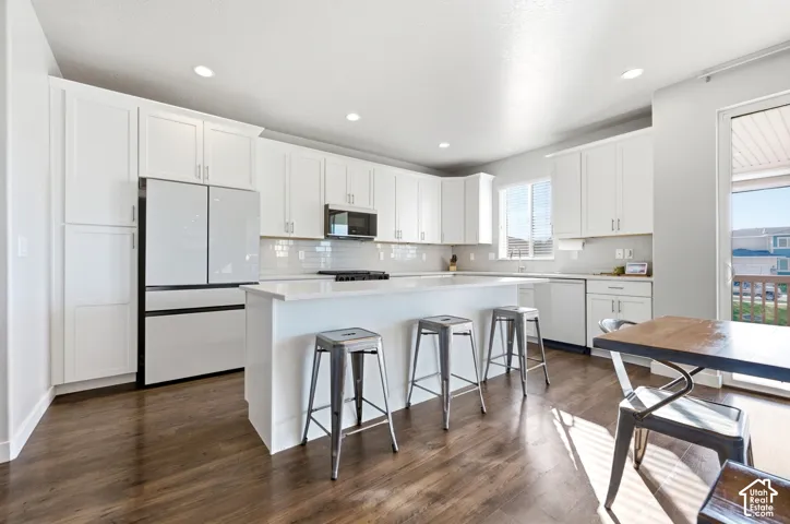 White cabinetry, wood-finish flooring, recessed lighting, central island, and sliding glass door