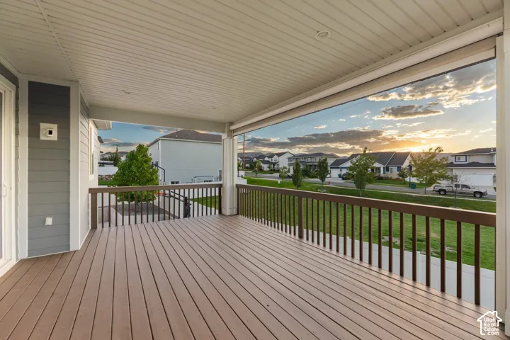 Covered deck featuring composite decking, white soffit ceiling, brown railing, and grey siding