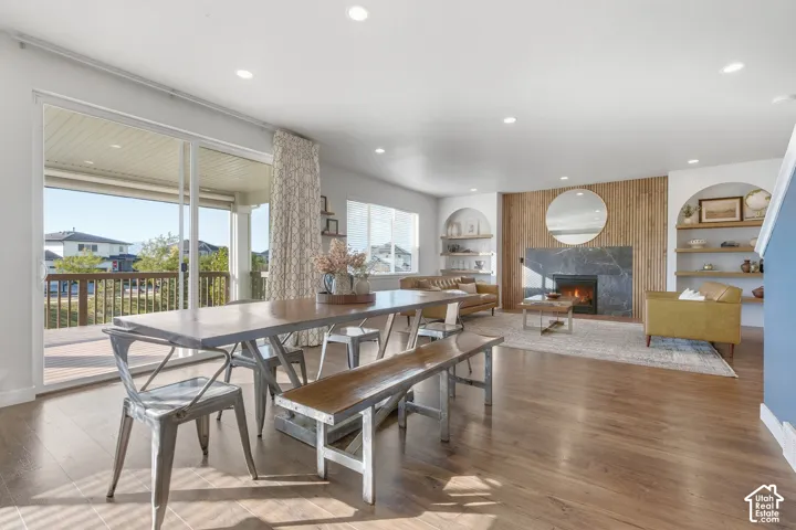 Sliding glass doors opening to a covered deck, wood-finish flooring, recessed lighting, and a fireplace with a stone surround and wood paneling