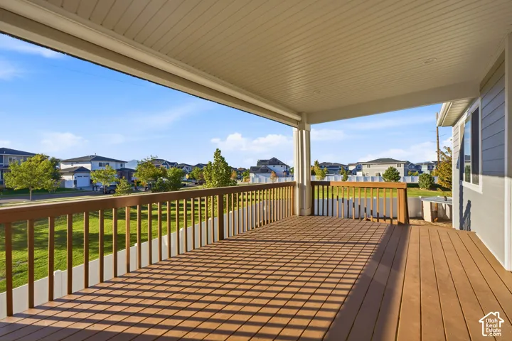 Expansive covered deck with wood-finish flooring, white railing, and exterior siding