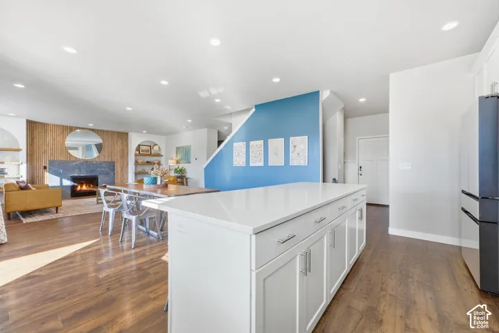 Modern open-concept kitchen and living space featuring a large white island with cabinetry and countertop workspace, recessed ceiling lighting, wood-finish flooring throughout, and an accent wall in soft blue with framed artw