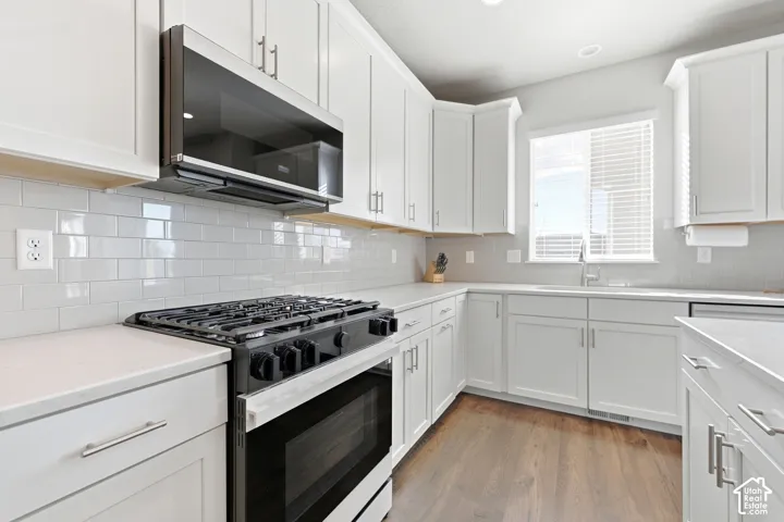 White shaker cabinetry, light-toned countertops, white subway tile backsplash, and wood-finish flooring
