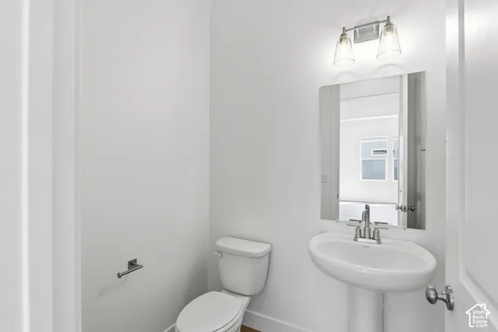Pedestal sink with a chrome faucet, wall-mounted mirror, and a two-bulb vanity light fixture