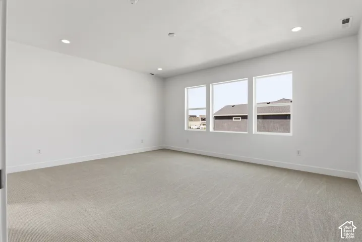 Spacious room featuring light-toned carpet, recessed lighting, and a wall of three large windows