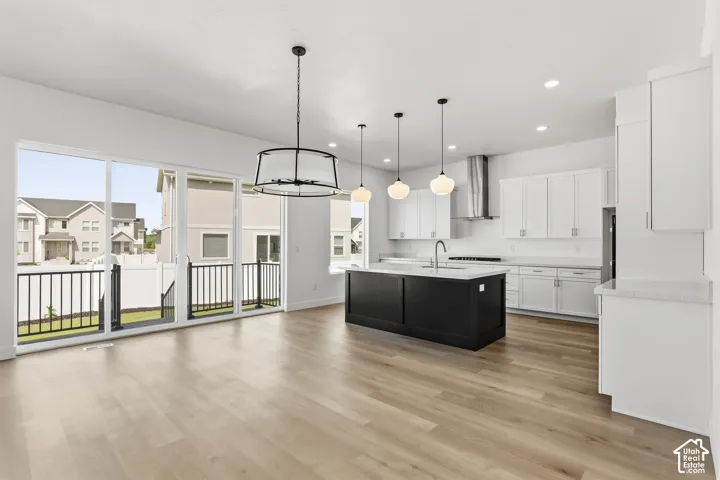 Open-concept living space featuring wood-finish flooring, a contemporary kitchen with white cabinetry, a black kitchen island, and stainless steel appliances