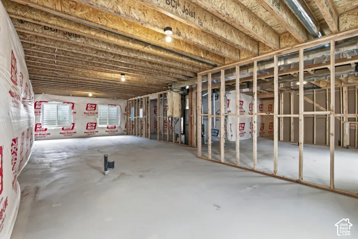 Unfinished basement featuring exposed wood joists, framed walls, a concrete floor, and two windows