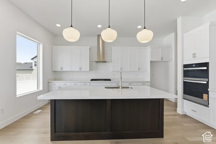 Contemporary kitchen featuring a spacious dark wood-finish island with a light-toned countertop, white cabinetry, integrated double ovens, and wood-finish flooring