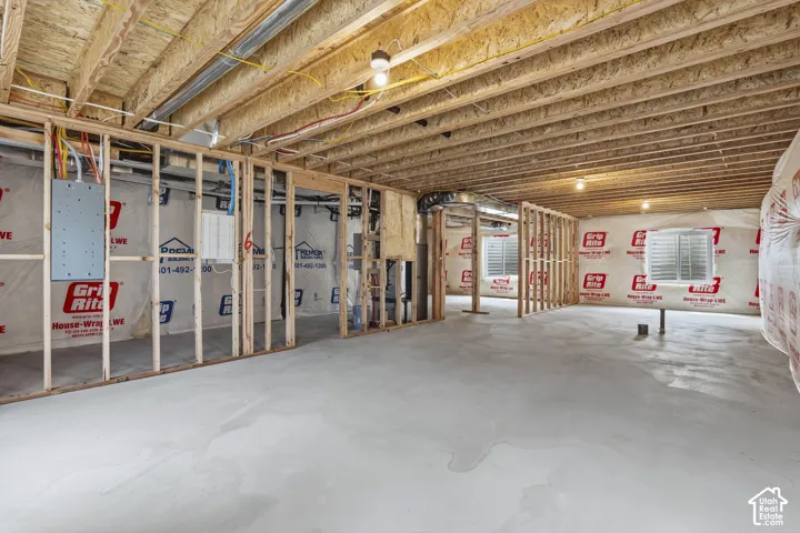 Unfinished basement with concrete flooring, framed interior walls, exposed ceiling joists, and multiple windows