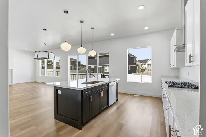 Spacious open-concept living area featuring wood-finish flooring, a kitchen island with pendant lighting, white cabinetry, integrated stainless steel appliances, and a gas cooktop