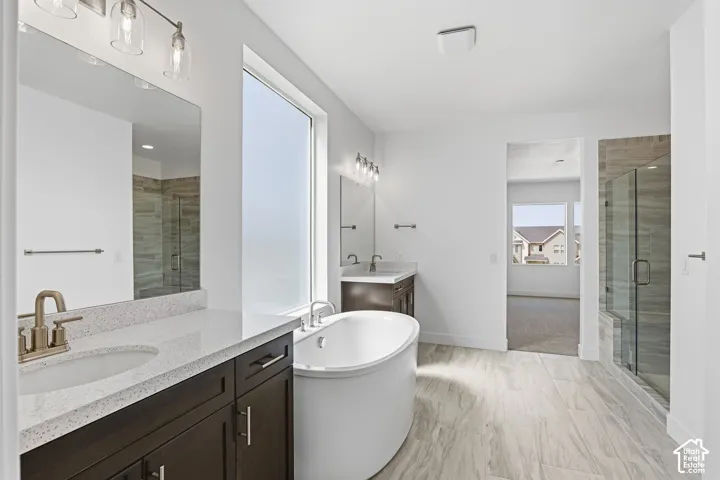 Dual vanity with undermount sinks, a freestanding soaking tub, a frameless glass shower enclosure, wood-finish flooring, and a large frosted window