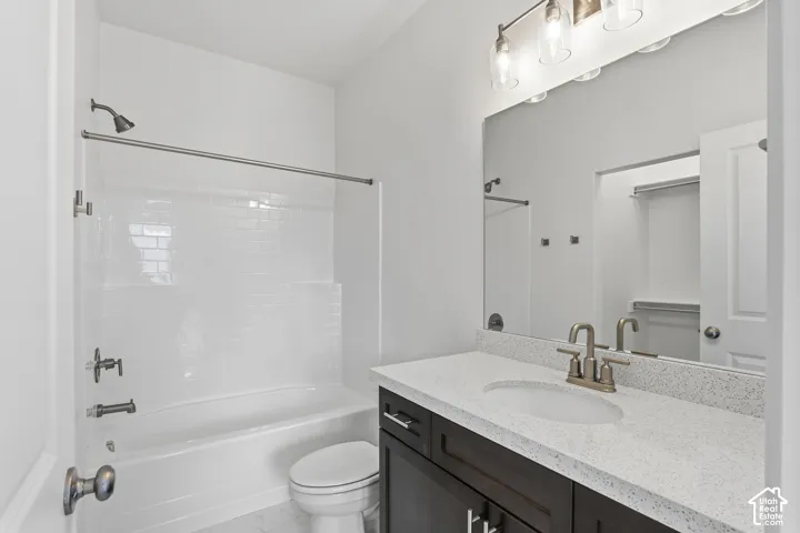 Bathroom featuring a dark wood-finish vanity, light speckled countertop, built-in mirror, three-light vanity fixture, and a shower/tub combination with subway tile surround