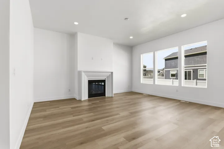 Spacious room featuring wood-finish flooring, a built-in fireplace with a white mantel, three large windows, and recessed ceiling lighting