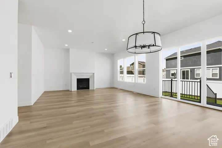 Expansive living area with light wood-finish flooring, a white mantel fireplace, and recessed ceiling lighting