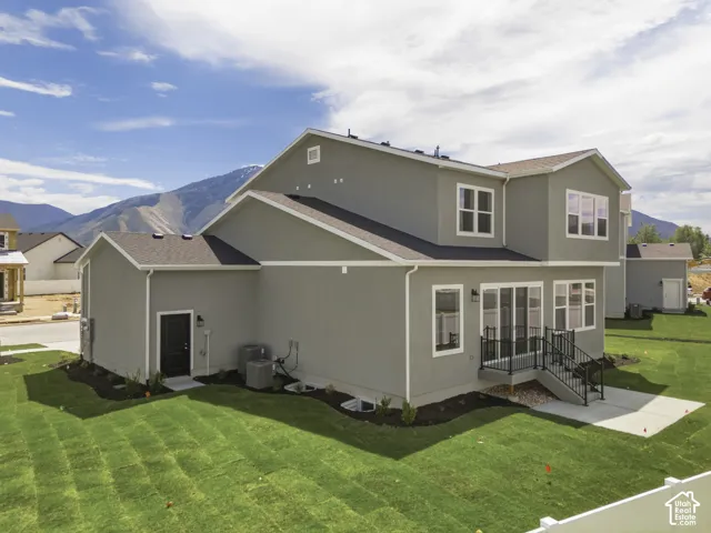 Expansive green lawn with mountain backdrop, concrete patio, sliding glass door, multiple windows, and exterior lighting
