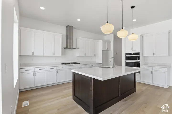 Spacious kitchen featuring white cabinetry, light countertops, wood-finish flooring, a central island with a sink, and stainless steel appliances