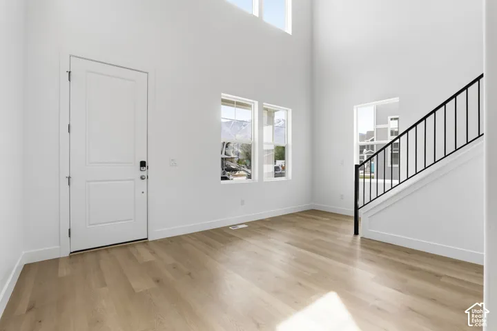 Soaring ceilings, wood-finish flooring, white walls, multiple windows, and a staircase with black metal balusters