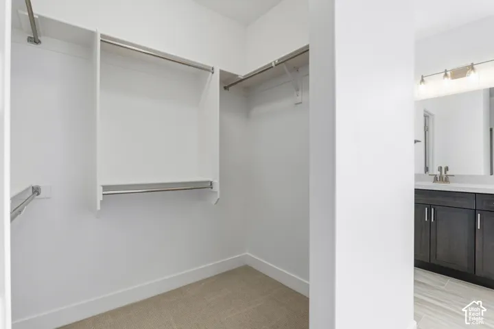 Built-in closet shelving with multiple hanging rods, accompanied by a bathroom vanity featuring dark wood-finish cabinetry, a light-colored countertop, and a large mirror with overhead lighting