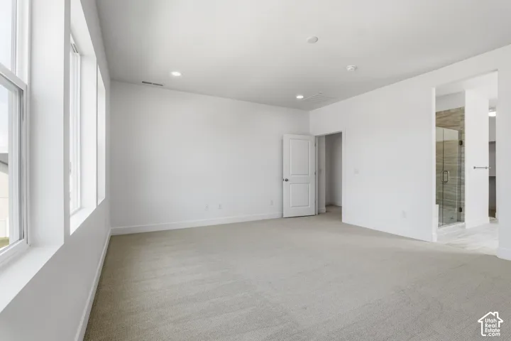 Spacious room featuring light-toned carpeting, multiple windows, recessed ceiling lighting, and an adjacent bathroom with a glass-enclosed shower