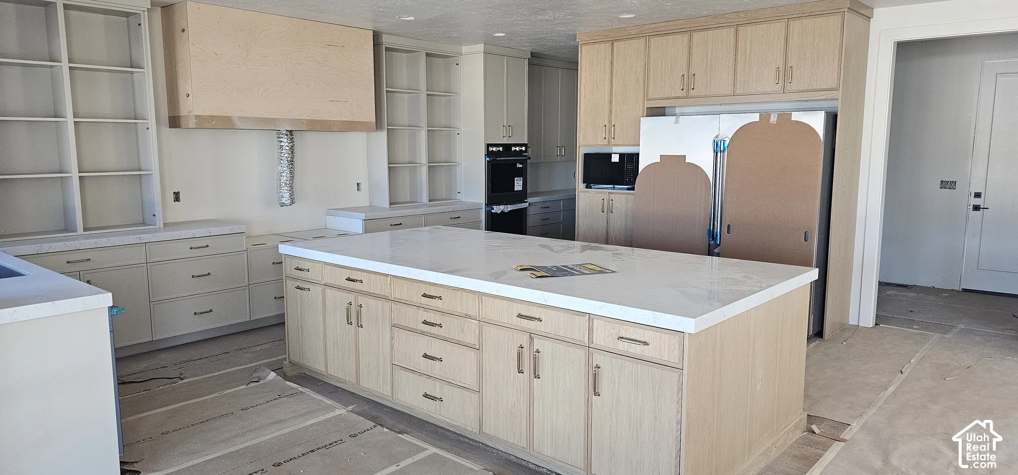 Spacious kitchen featuring a large central island with a light-toned countertop, extensive light wood-finish cabinetry, and built-in shelving