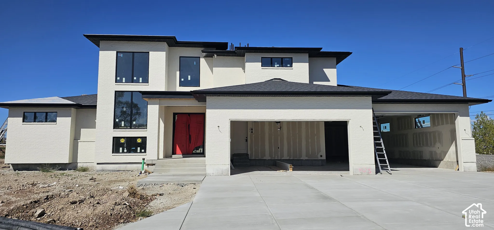 Contemporary exterior with a light-toned facade, black-framed windows, a prominent red entry door, an attached garage, and a concrete driveway