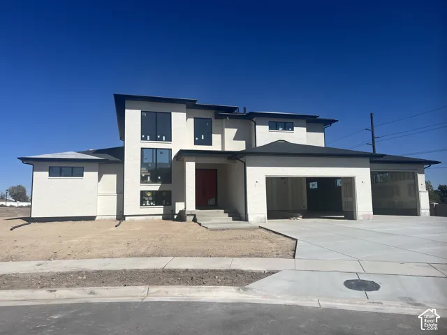 Contemporary exterior featuring a light-colored facade, multi-paned windows, a prominent red entry door, a multi-car garage, and a concrete driveway