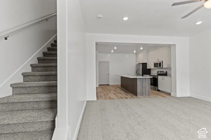 Open concept living space featuring a carpeted staircase, recessed lighting, and a modern kitchen with an island, stainless steel appliances, and light-toned cabinetry