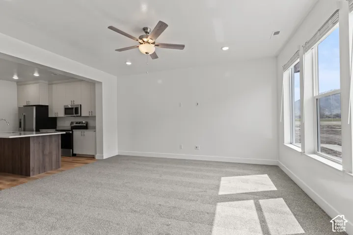 Open-concept living area with grey carpeting and a ceiling fan
