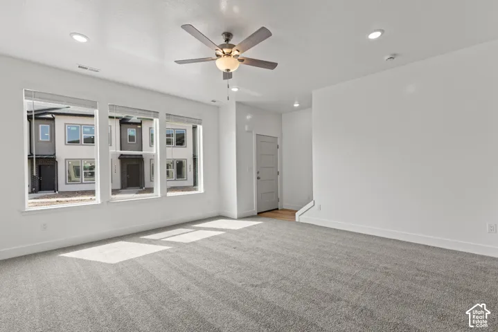 Spacious room featuring multiple windows, recessed lighting, ceiling fan, carpet flooring, and a panel door