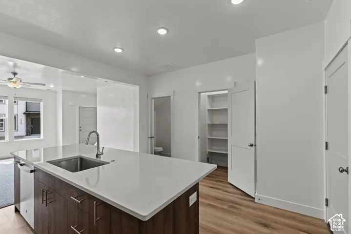 Kitchen island with an undermount sink and a stainless steel faucet, wood-finish flooring, recessed lighting, white cabinetry, and a pantry with shelving