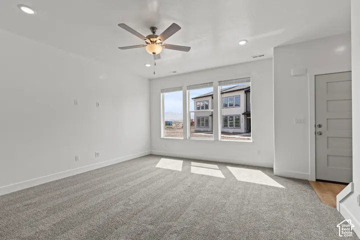 Carpeted living space with a ceiling fan, recessed lighting, and a multi-panel door with a lever handle