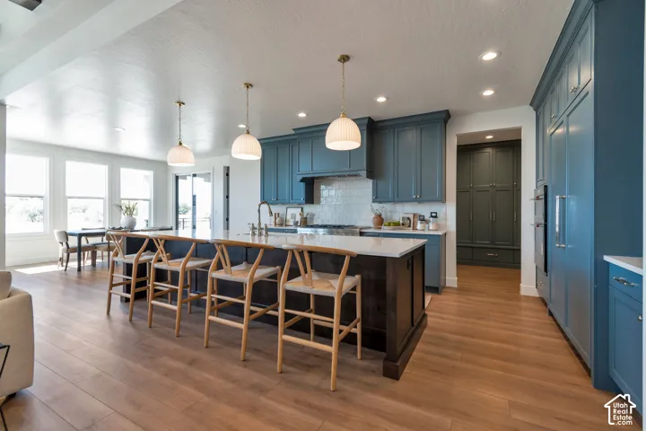 Expansive kitchen featuring wood-finish flooring, a large central island with seating, pendant lighting, built-in appliances, and abundant cabinetry