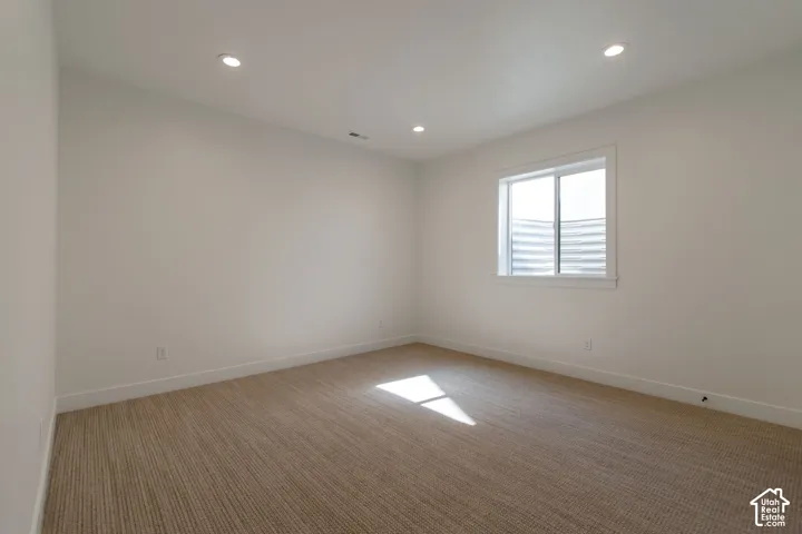 Neutral wall paint, recessed lighting, white window trim, and textured carpet flooring
