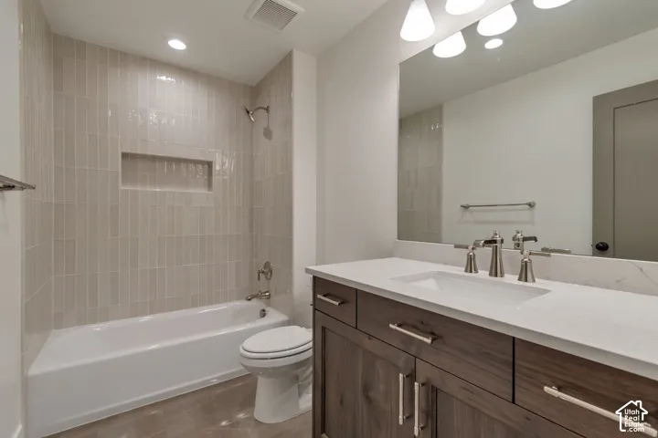 Integrated bathtub and shower with vertical tile surround, recessed shower niche, single vanity with wood-finish cabinetry, quartz countertop, and brushed nickel fixtures