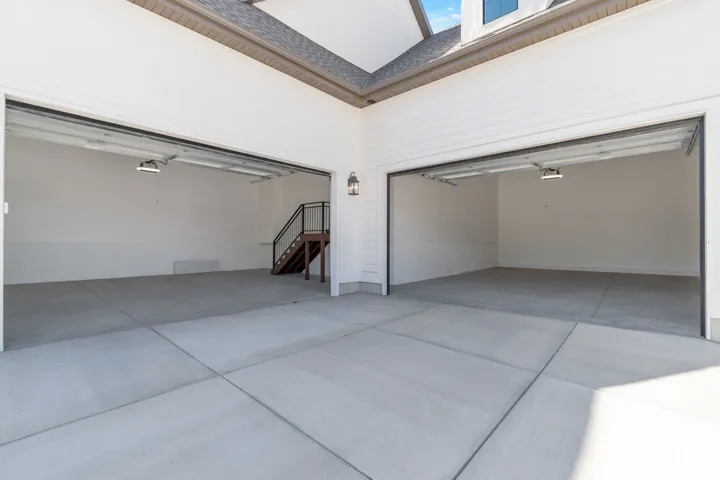 Two-car garage with concrete flooring, illuminated by overhead lighting and an exterior wall lantern