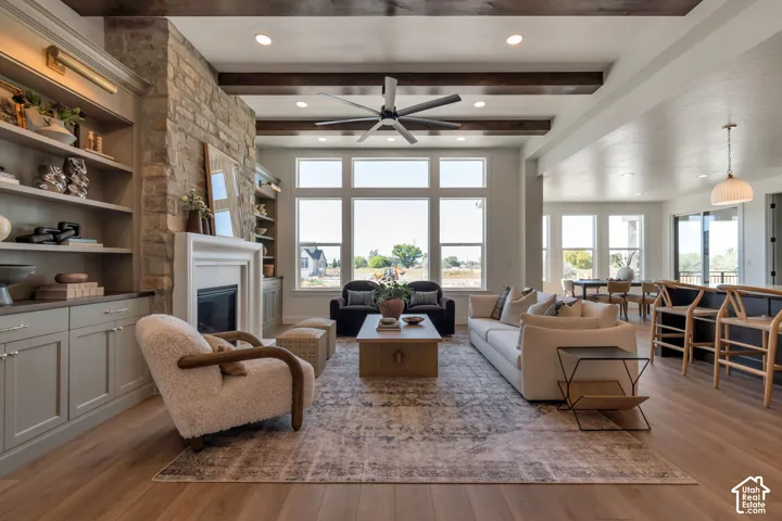 Living area featuring wood-finish flooring, a stone-clad fireplace, built-in shelving, exposed ceiling beams, and recessed lighting