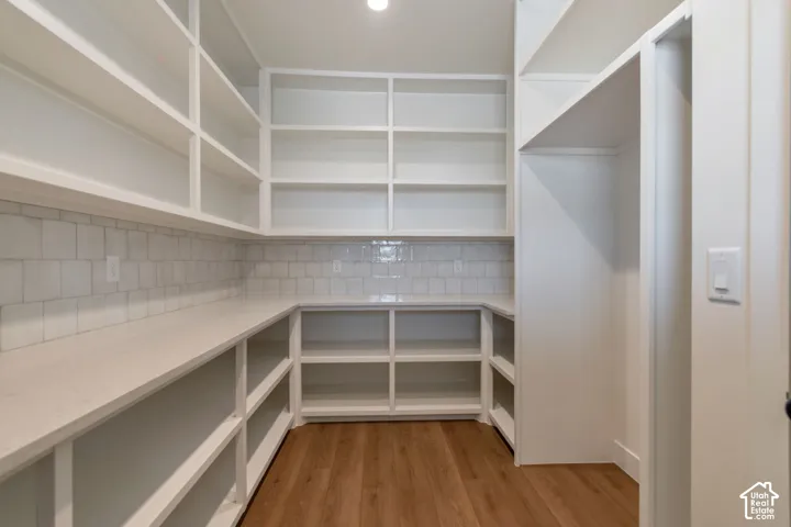 White built-in shelving, extensive counter space, subway tile backsplash, wood-finish flooring, and recessed lighting