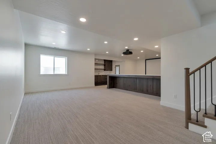 Expansive open-concept room featuring recessed lighting, a built-in wet bar with dark wood-finish cabinetry, a large projection screen, and a staircase with wood-finish handrails and black metal spindles