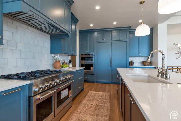 Expansive kitchen with blue cabinetry, stainless steel range with double ovens, integrated refrigerator, white subway tile backsplash, and wood-finish flooring