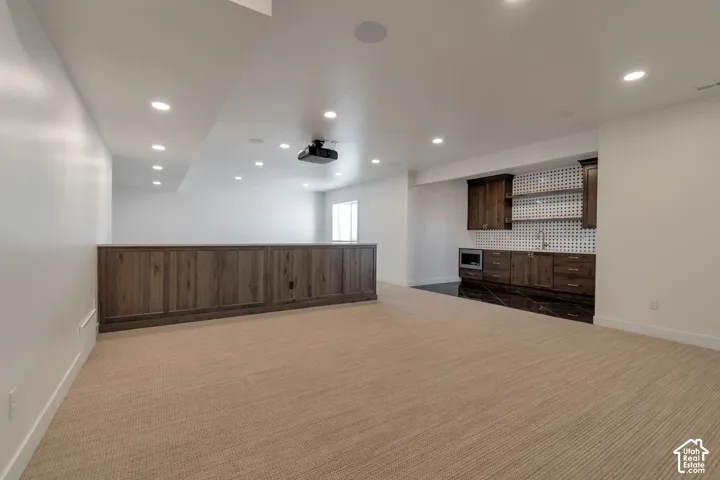 Recessed lighting throughout, built-in projector, wood-paneled half-wall, integrated wet bar with dark wood cabinetry, and polished dark flooring