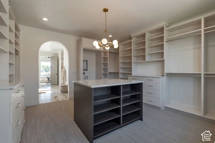Spacious custom closet featuring a central island with countertop, abundant built-in shelving, integrated drawers with polished hardware, and recessed lighting