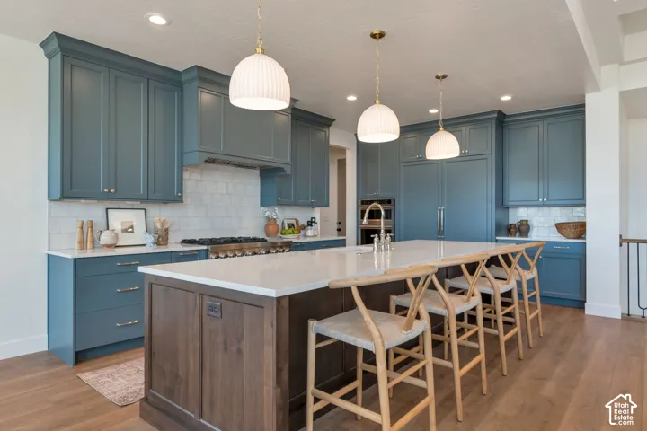Spacious kitchen featuring extensive blue cabinetry, a large center island with a light-toned countertop, wood-finish flooring, and pendant lighting