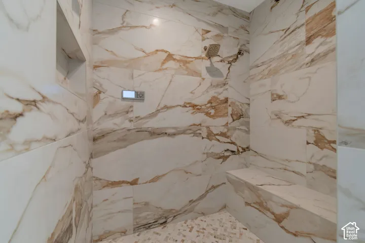 Shower featuring large format tile with naturalistic veining, mosaic tile flooring, built-in shelving, a built-in bench, and a modern showerhead