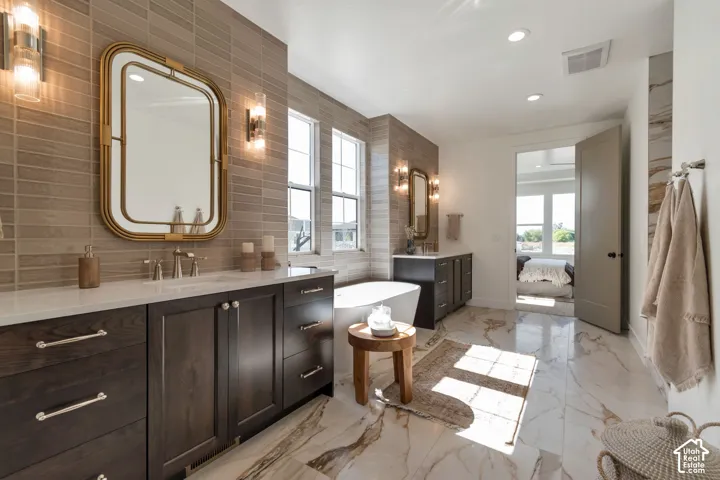 Dual dark wood vanities with white countertops, freestanding soaking tub, and marble-finish flooring