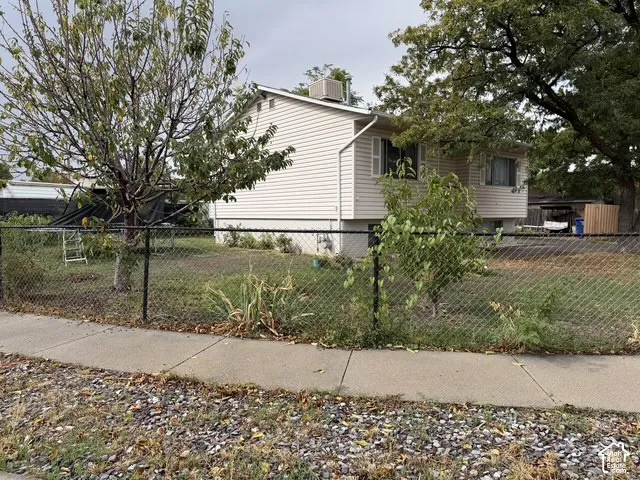 Vinyl siding exterior with a chain link fence, mature trees, and a concrete sidewalk