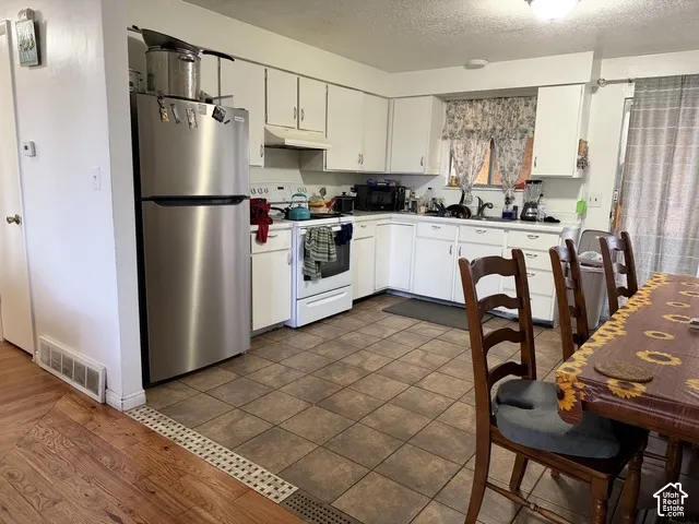 Kitchen featuring white cabinetry, tile flooring, stainless steel refrigerator, and a window above the sink