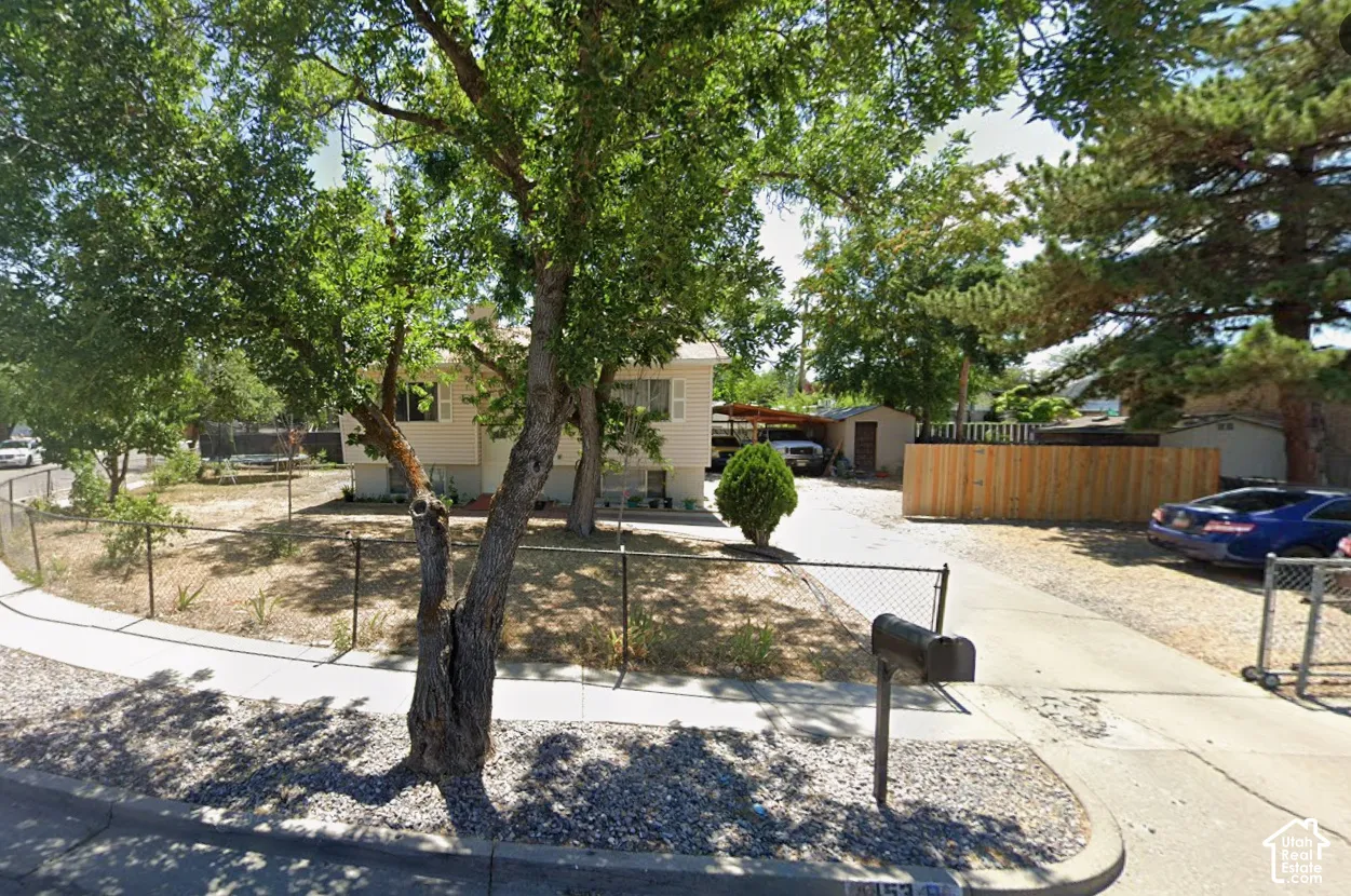 Corner lot featuring a chain-link fence, mature trees, and a gravel driveway