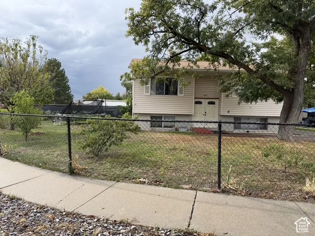 Two-story exterior with light-colored siding, a prominent mature tree, and a black chain-link fence