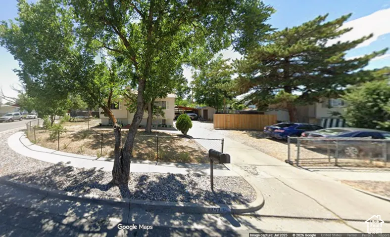 Spacious corner lot with established trees, a concrete driveway, and a wood fence