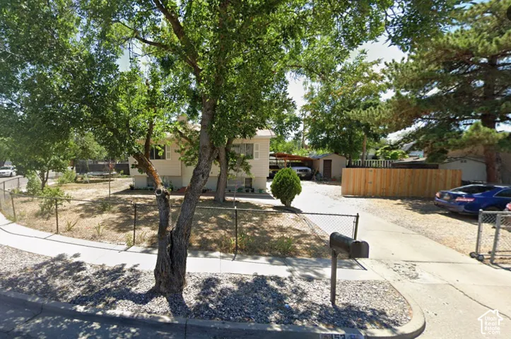 Corner lot featuring a chain-link fence, mature trees, and a gravel driveway