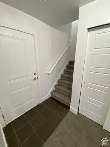 Tiled entry flooring, paneled interior doors, and carpeted stairs with a white handrail